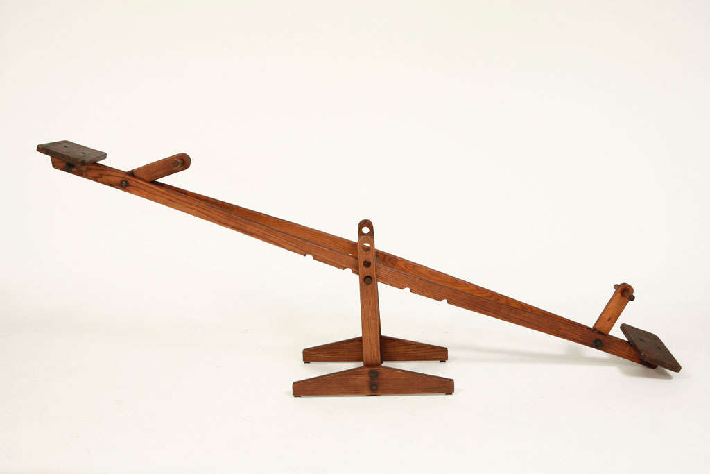 Simple and raw vintage wood teeter totter with carved notches at center to adjust height, small wood seats at ends of narrow board, and pivoting hand grips.