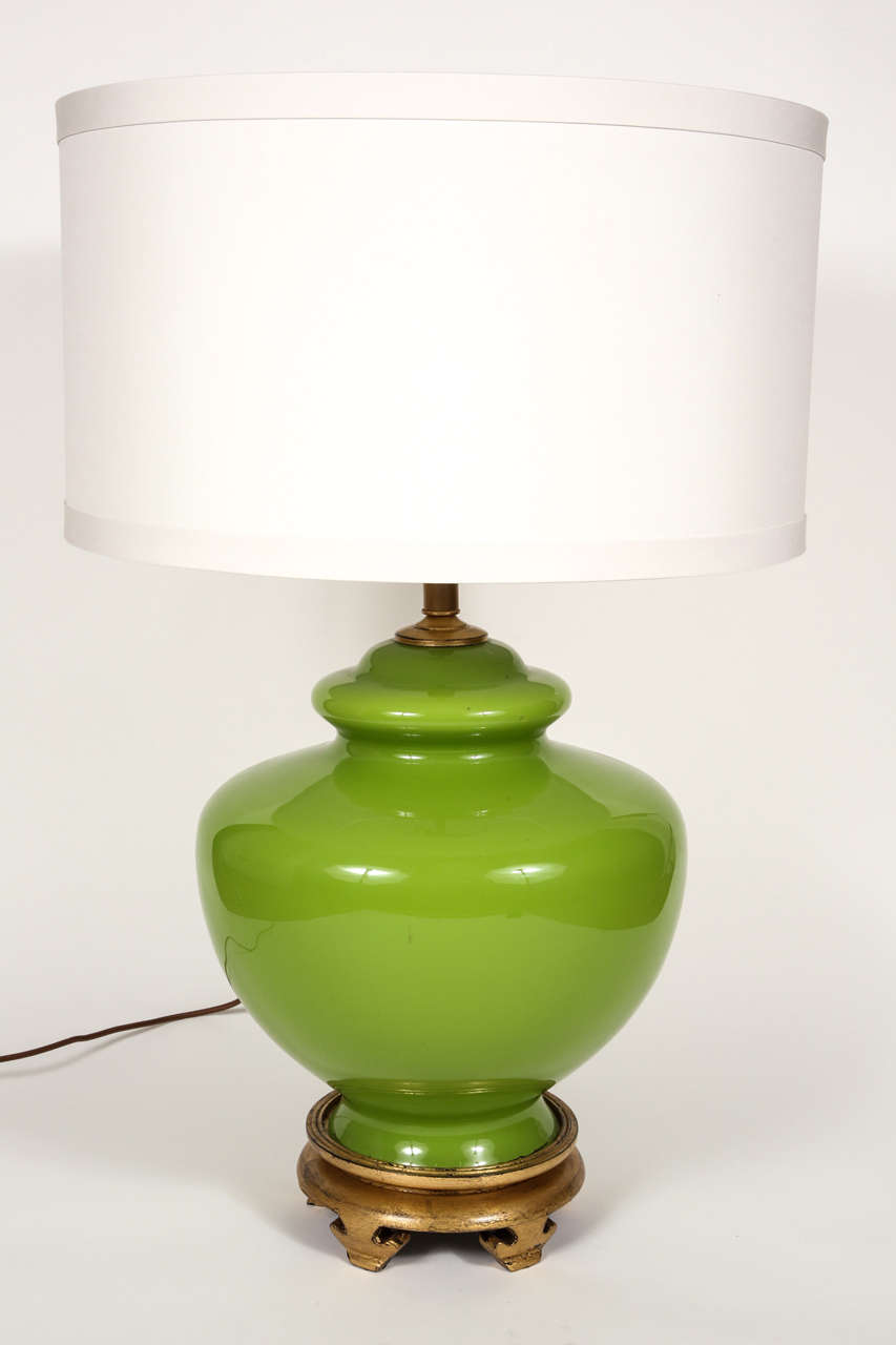 Chartreuse green urn shaped glass lamp.  Gilded wooden base with brass hardware.  Two-lights with independent switches.  Custom drum shade.  22 1/2