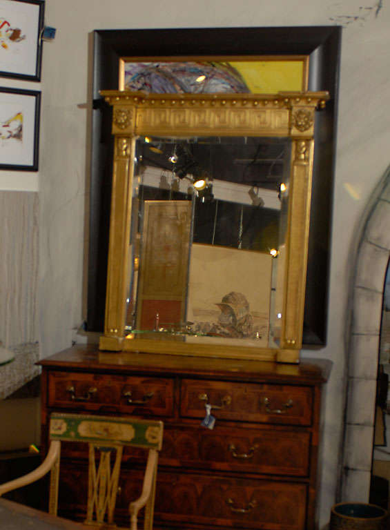 A carved gilt wood and composition over mantle mirror, the ball and molded ribbon crest above a frieze decorated with Greek key and lion heads above sphinx caryatids.  The mirror glass has been replaced.