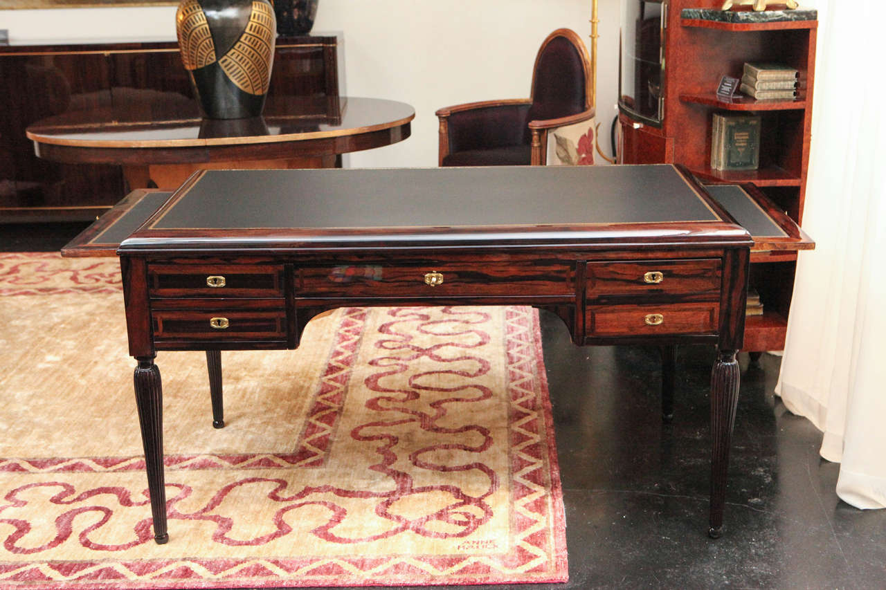 Stunning desk in Macassar ebony by Maurice Jallot. Black leather top with gold Greek Key border and pull-out shelves. Flower marquetry detailing on front of desk and hand-carved fluted legs. Matching desk chair available in open barrel style in