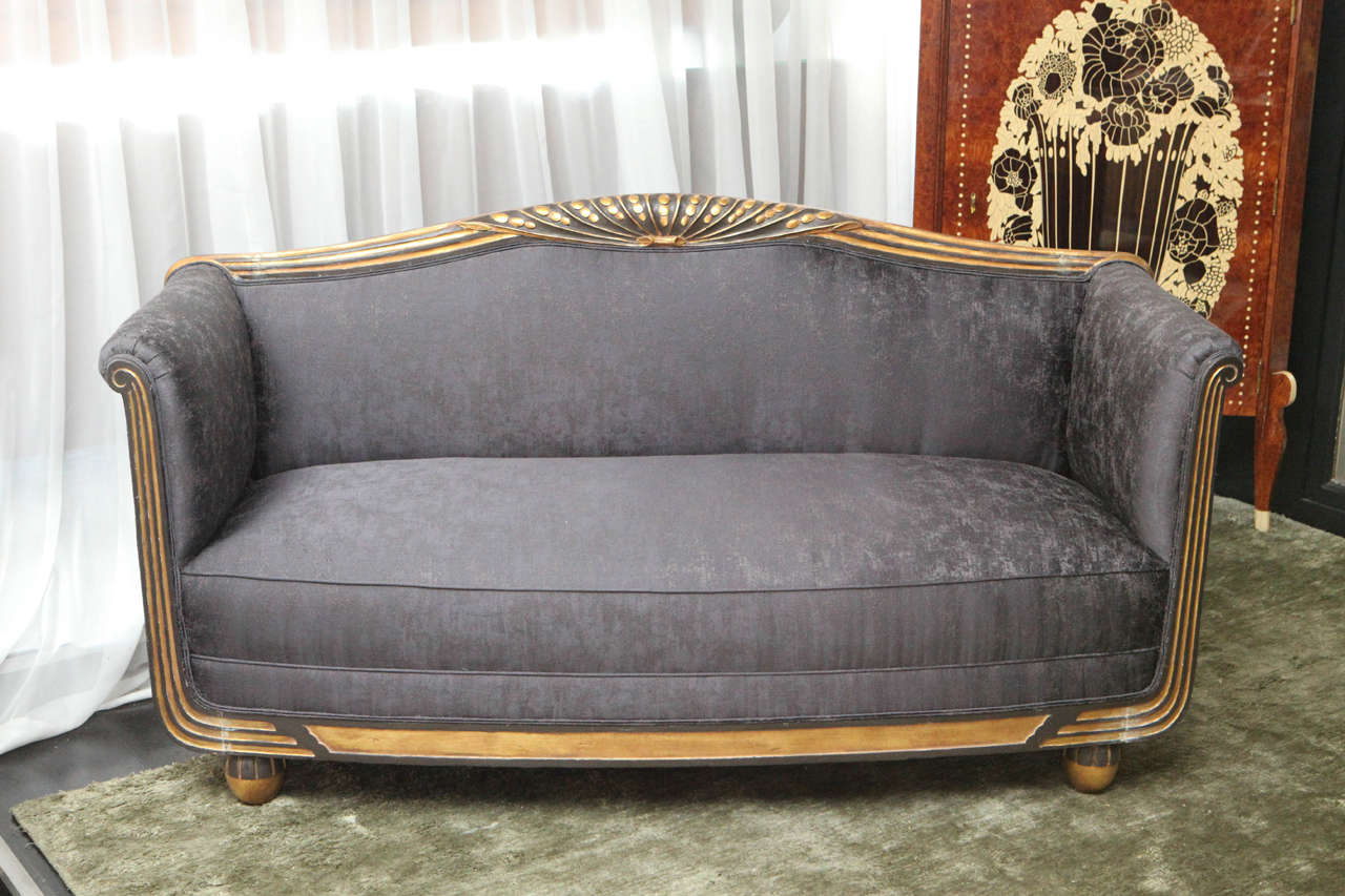 Art Deco sofa with relief carving along the frame and ball feet in gold leaf. A stylized flower motif along the back with antiqued paint and gold leaf. Textured grey linen/silk upholstery.