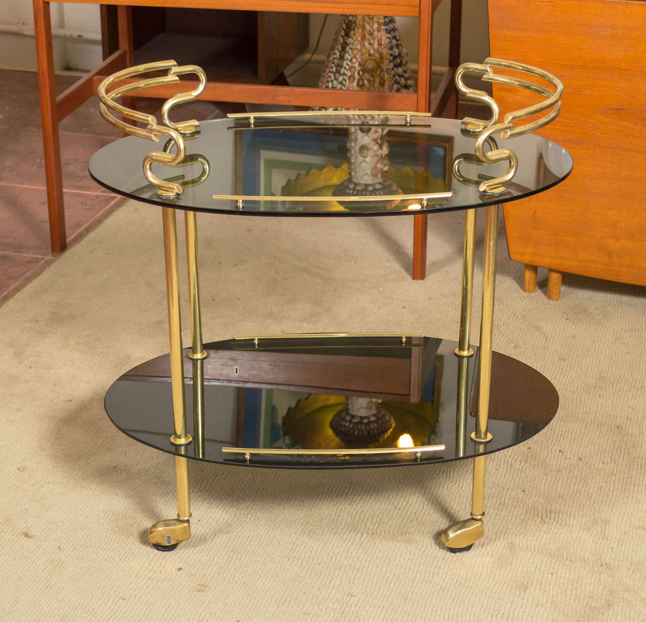 Just stunning, wonderful curves on this, circa 1960s, bar or serving cart, two oval shelves of smoke glass, with the metal work brass. Wheels are rubber so you have easy gliding across the room.