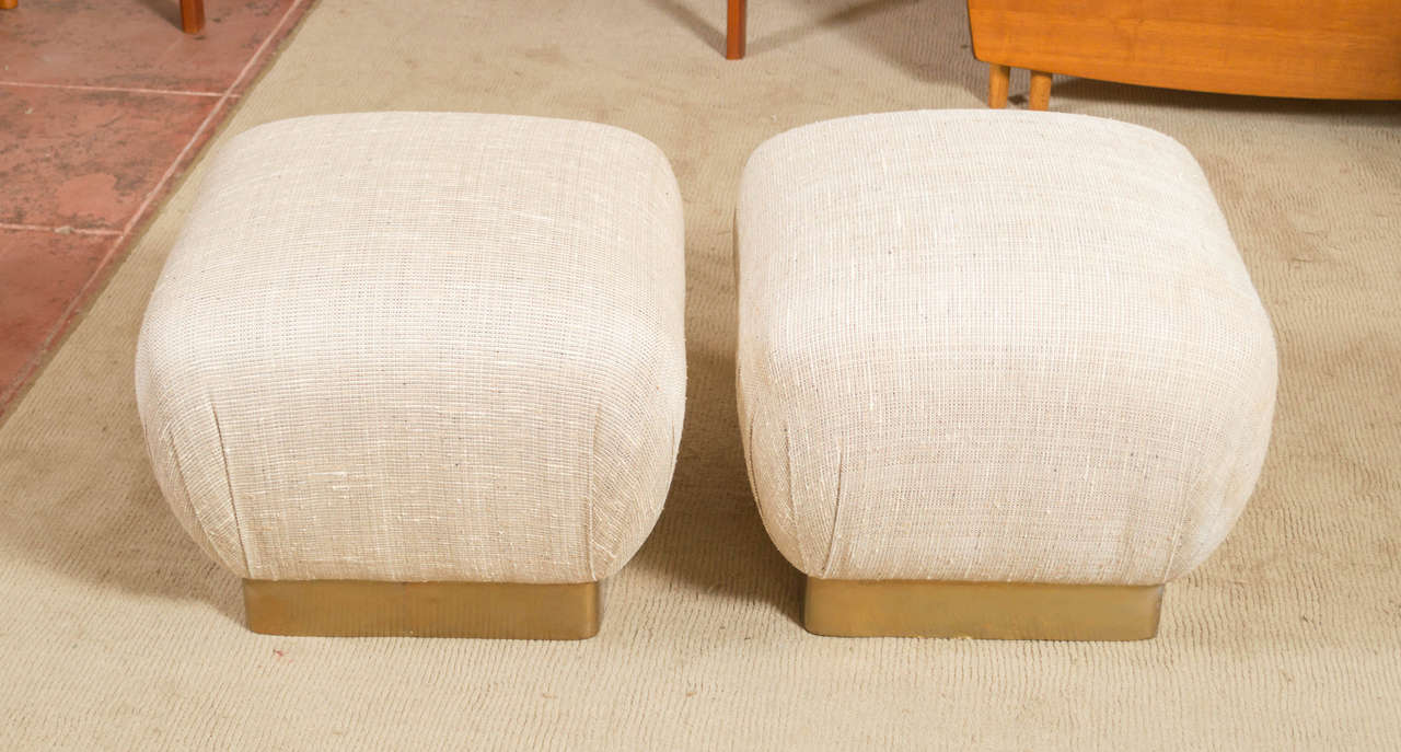 A pair of poufs/ottomans by Marge Carson. A Brass sheet around their bottoms and with their cushion popping up like a soufflé. A great set for some extra seating at your next cocktail party.