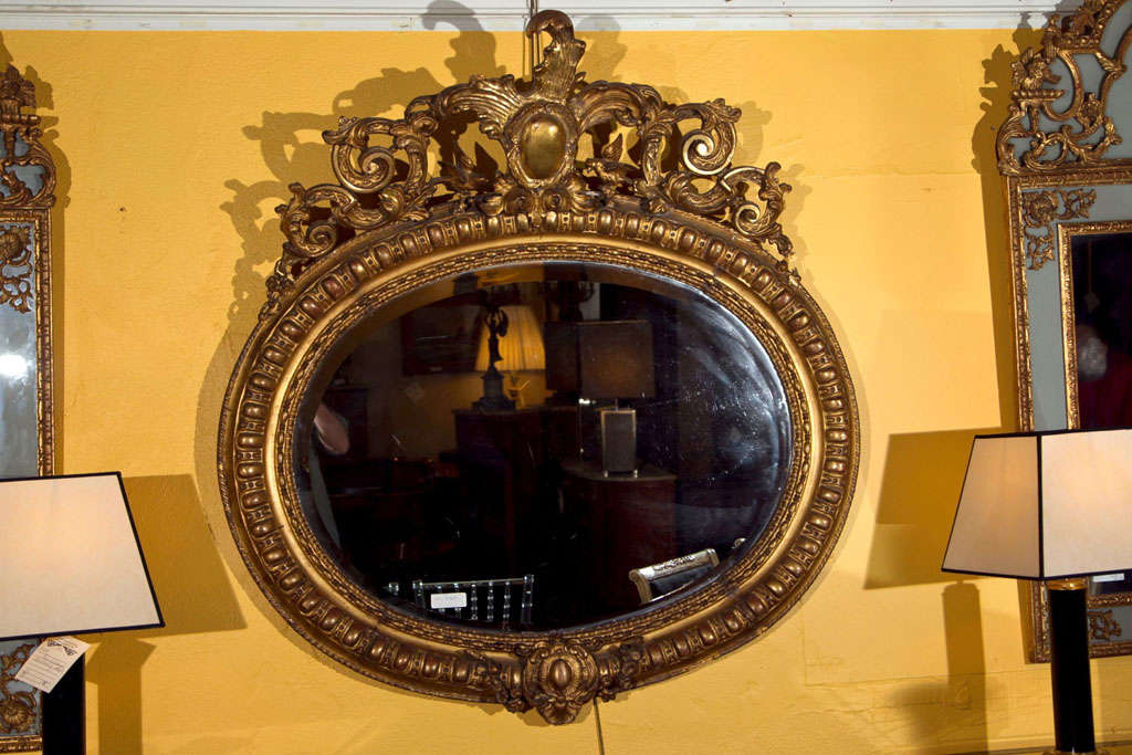 A French giltwood mirror, late 19th possibly early 20th century, the oval annular frame centered by ornately carved crest of foliate, scrolls and birds.