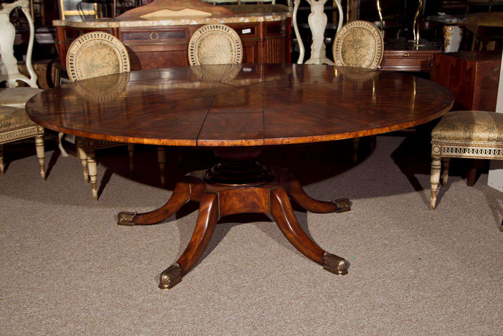 A magnificent metamorphic mahogany with satinwood and ebony inlaid banding circular dining table, mid 20th century, this table is finely designed to have folded hidden leaves extending to a wider surface, raised on a single pedestal, supported by