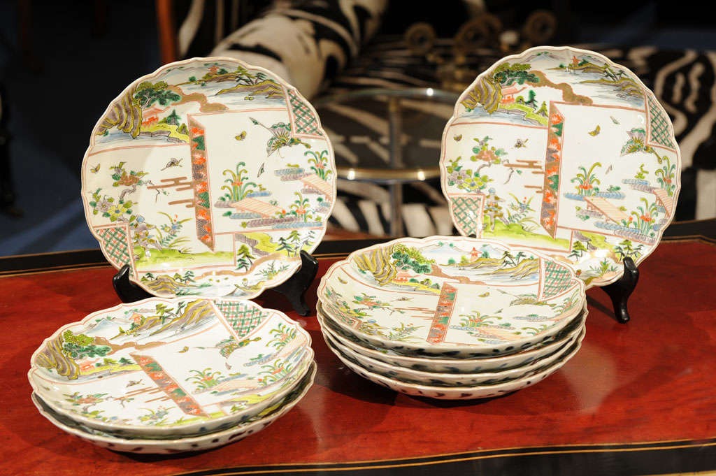 Each deeply formed circular plate with scalloped rims trimmed in gilt and decorated with overlapping scenes of blooming gardens and mountainous landscapes.