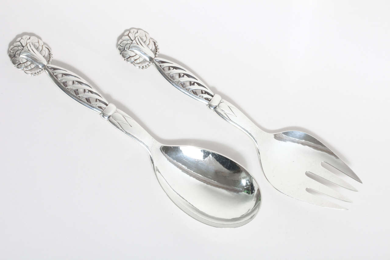 A sterling silver spoon and fork salad server designed by Georg Jensen (1866-1935) in 1914 with openwork handles.
Hallmarks: Georg Jensen (1945-present mark)/ sterling / Denmark / 83.

Measures: Serving spoon: Length 9.5'', width 2 5/8''
Serving