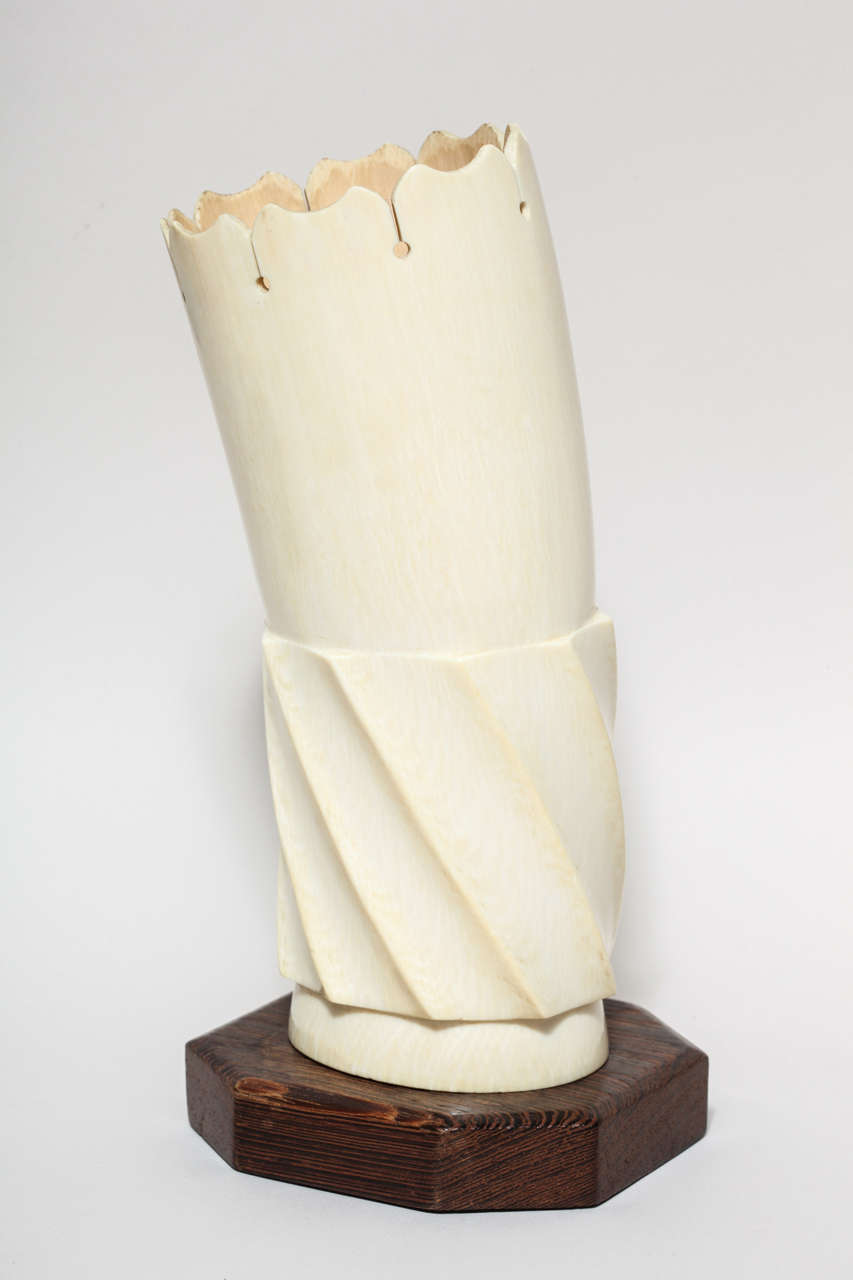 Sculpted bone vase with the lower half a fluted spiral and mounted on a wood base.