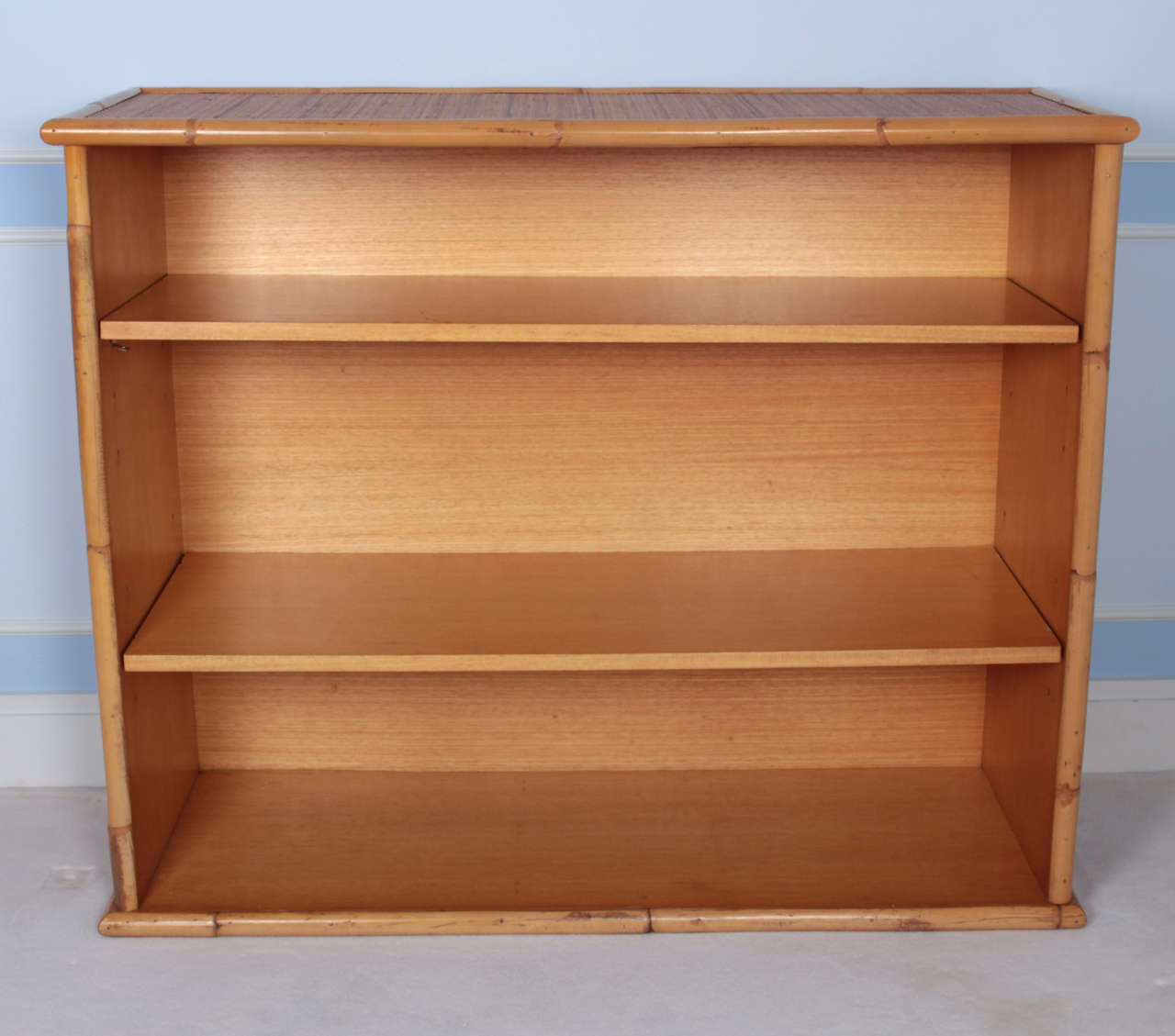 Pair of low and wide bookcases with fixed shelves, bamboo frames, rattan panels on sides and top.