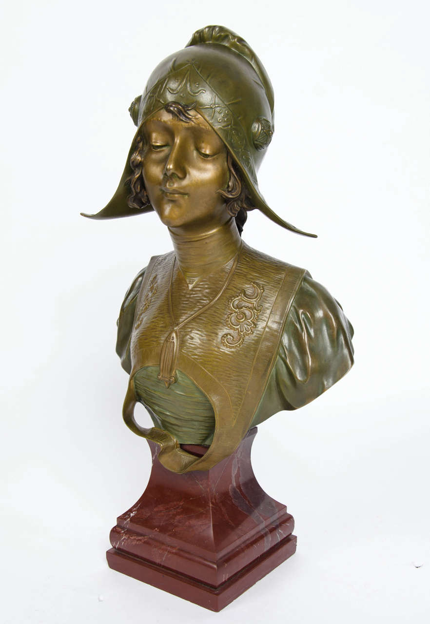 An Art Nouveau bronze bust by Henri Jacobs (1864-1935). A study of a young girl in demure pose wearing traditional dress. Golden, green patination and charing characterization. Set on a red marble plinth.

Signed H Jacobs to bronze and marked for