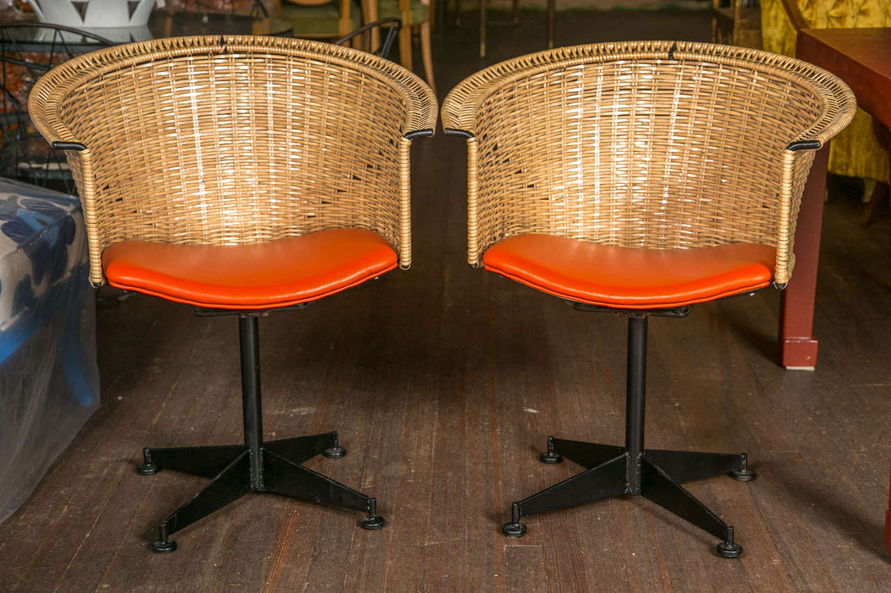 Pair of black  iron swivel chairs with protectively wrapped rattan backs and orange vinyl seats. Seat height is 17.5