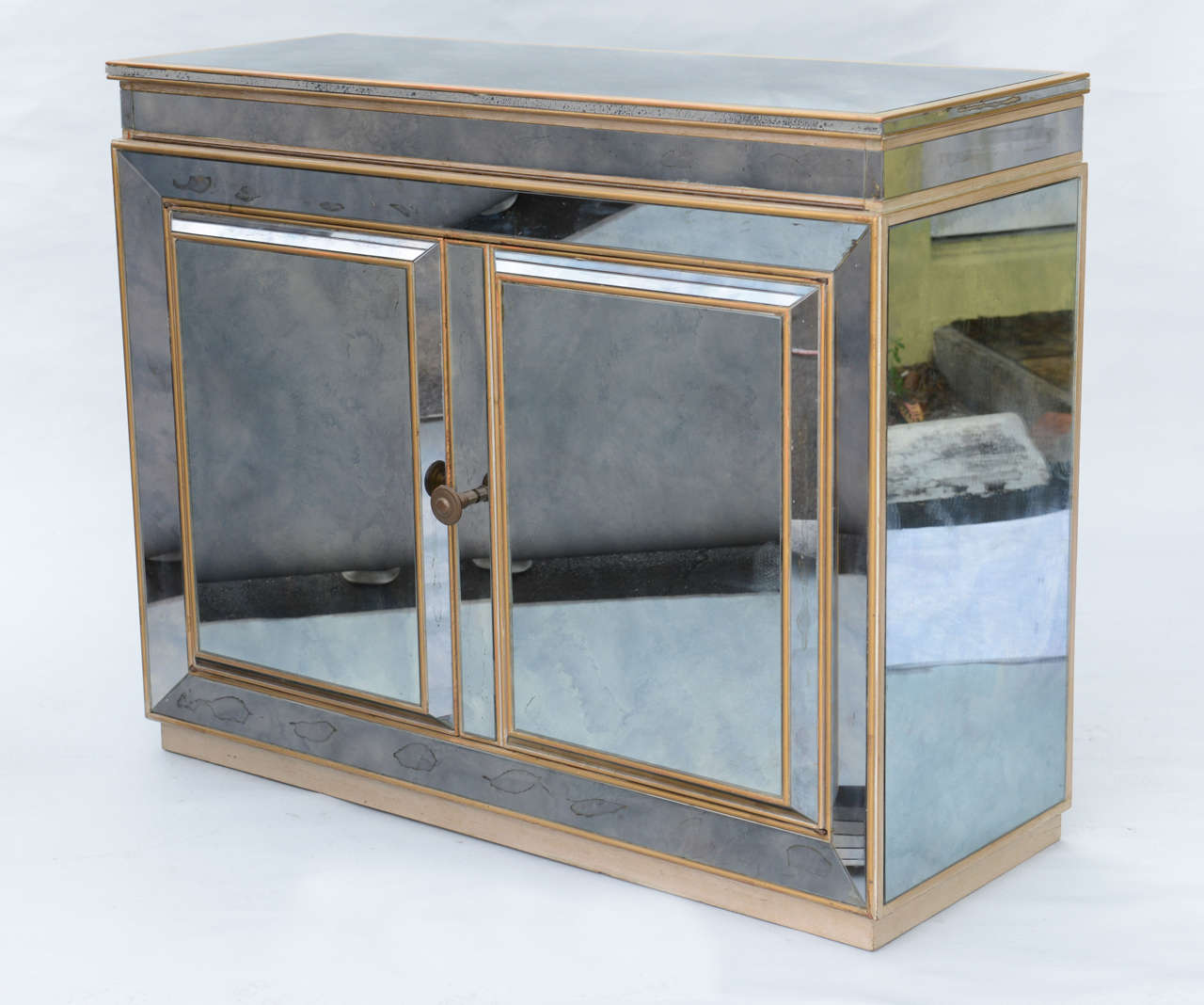 Bar cabinet, its surfaces entirely covered with smoked and spotted mirrorplate with giltwood trim; its hinged lid opens to reveal cutouts for bottles and glassware, two lower cupboard doors with shelf.

(keywords: Buffet, Sideboard, Server, Dry