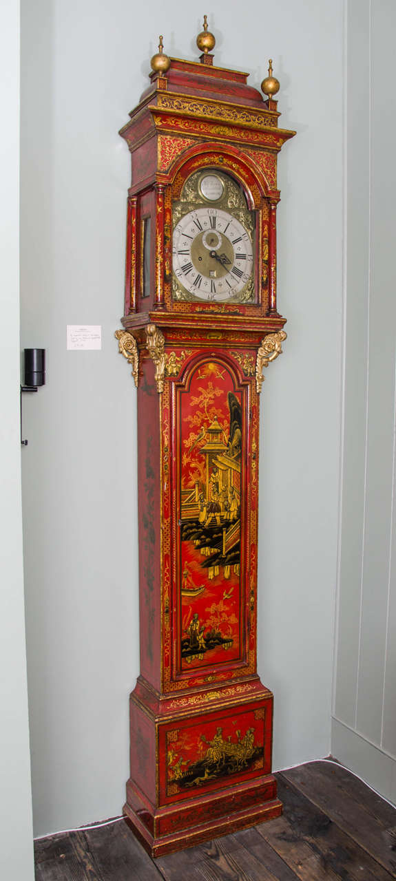 By Jno. Austin of Shoreditch, London. The unusual red lacquer case is decorated in low relief with a gilt landscape vignette on the door and a stylised picnic on the plinth. The movement is supported on gilt scroll brackets and the domed pediment is