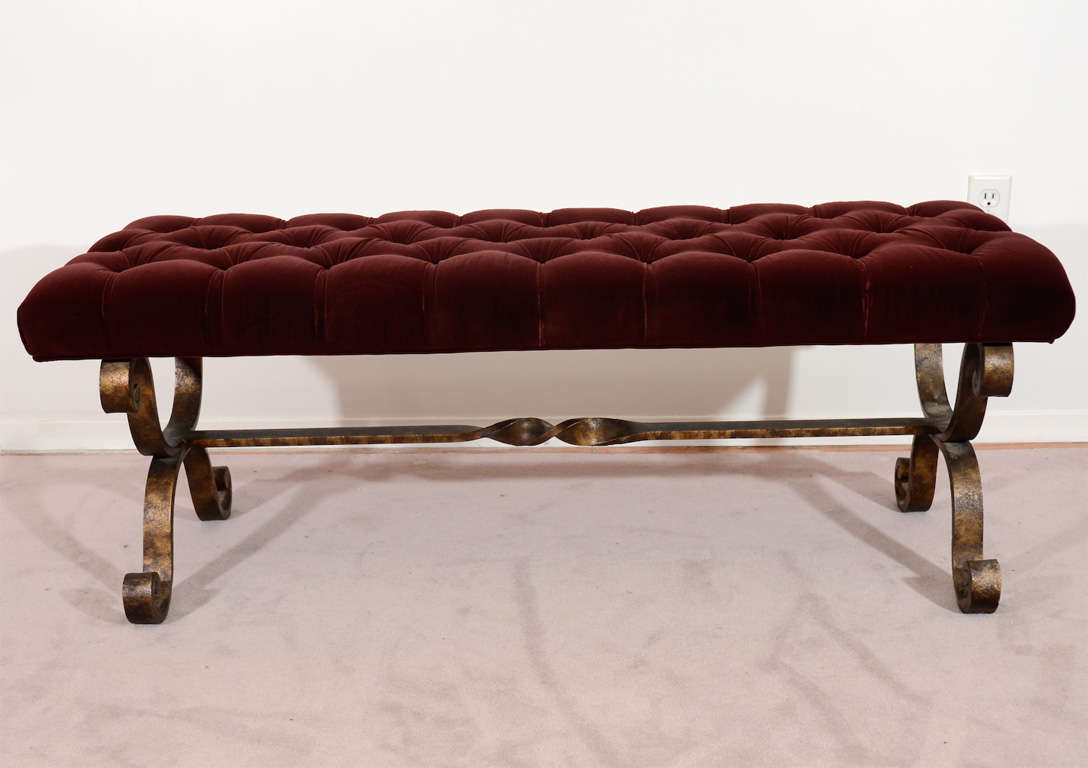 A vintage bench with a scrolled, patinated iron base and tufted burgundy cushion. The piece has been recently reupholstered