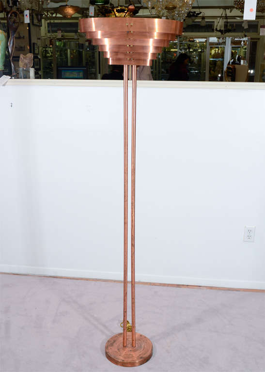 An Art Deco modernist floor lamp in copper. The piece consists of a circular copper base supporting two tubular rods ending with a tiered sheet copper shade. The piece is by noted designer Kurt Versen.