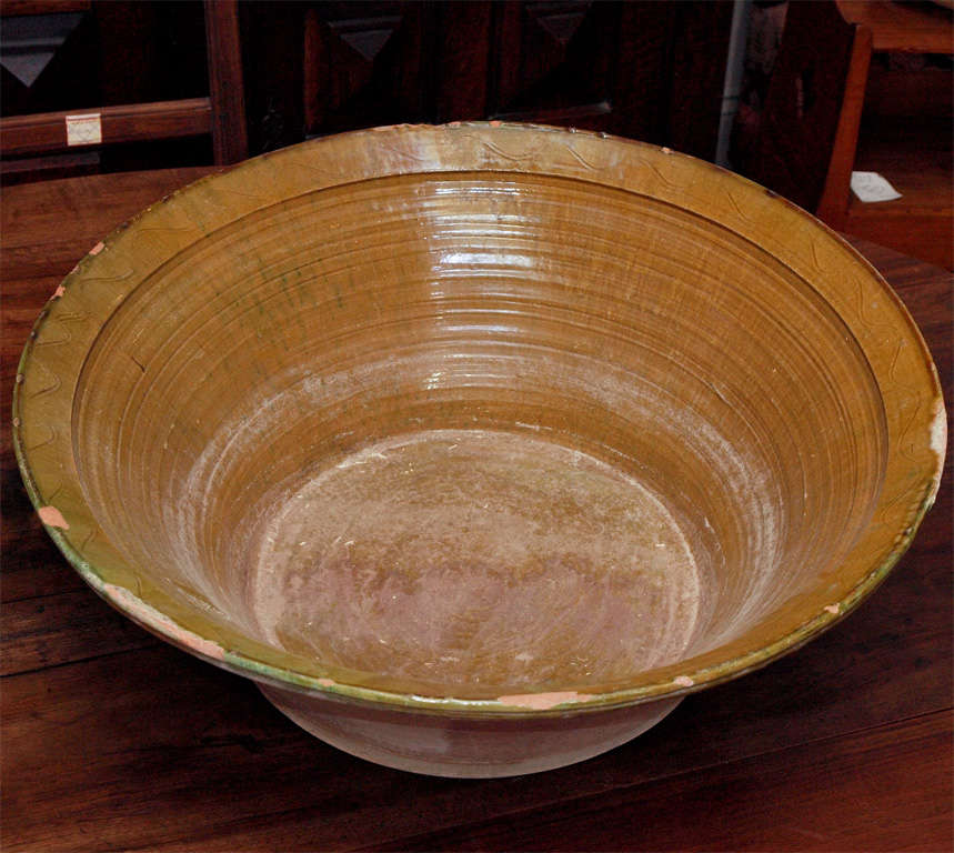 Large terracotta flat bottom bowls, or basins, known as lebrillos; having glazed interiors and rims with incised decoration.  One bowl with an ochre glaze, the other a yellow-green.