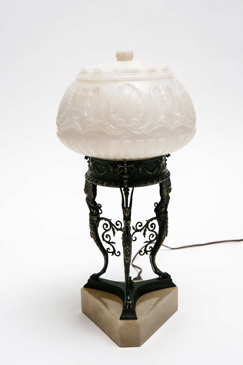 A striking cast bronze and alabaster accent lamp after the ancient Greek. The bronze base features a trio of winged griffins, pad feet and scrollwork and is set on a honey onyx base. The alabaster shade features carved details including feathers and