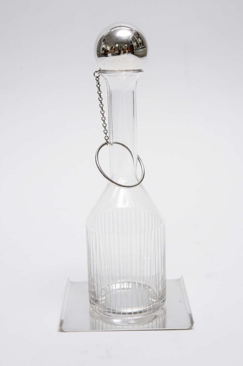 A chic etched crystal decanter set on a silver plate tray with turned up edges and topped with a ball and chain stopper. The decanter itself measures 4