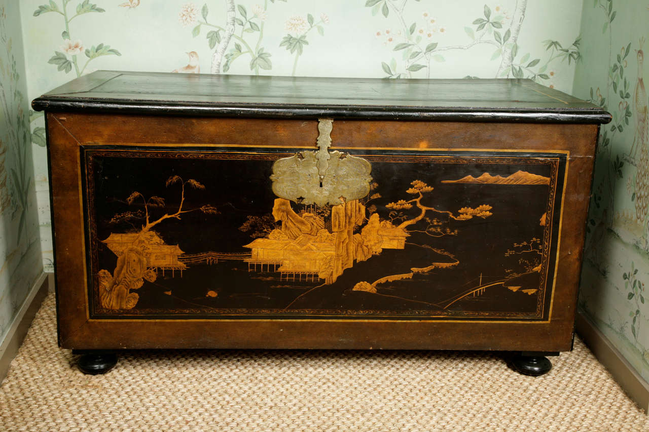 A continental Japanned trunk, early 18th century. Decorated in the Japanese taste with elaborate lock escutcheon and solid brass handles. On ebonized bun feet. The large central front panel showing an Oriental landscape, decorated sides and the back