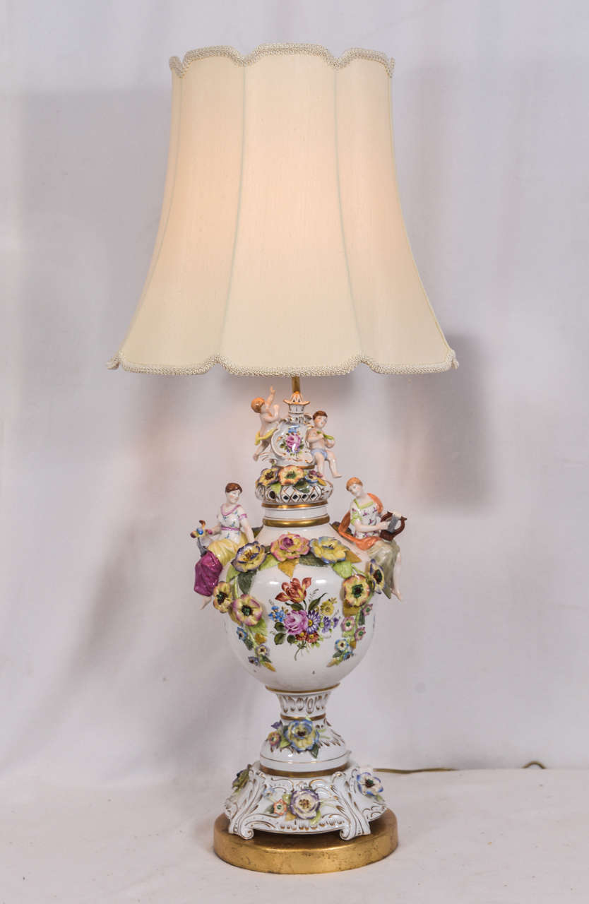 German porcelain urns as lamps, with flowers, cherubs, beautiful maidens, in hand-painted, sculptured porcelain, priced without lampshades. Shades shown are off-white silk, v-notched frame, 16