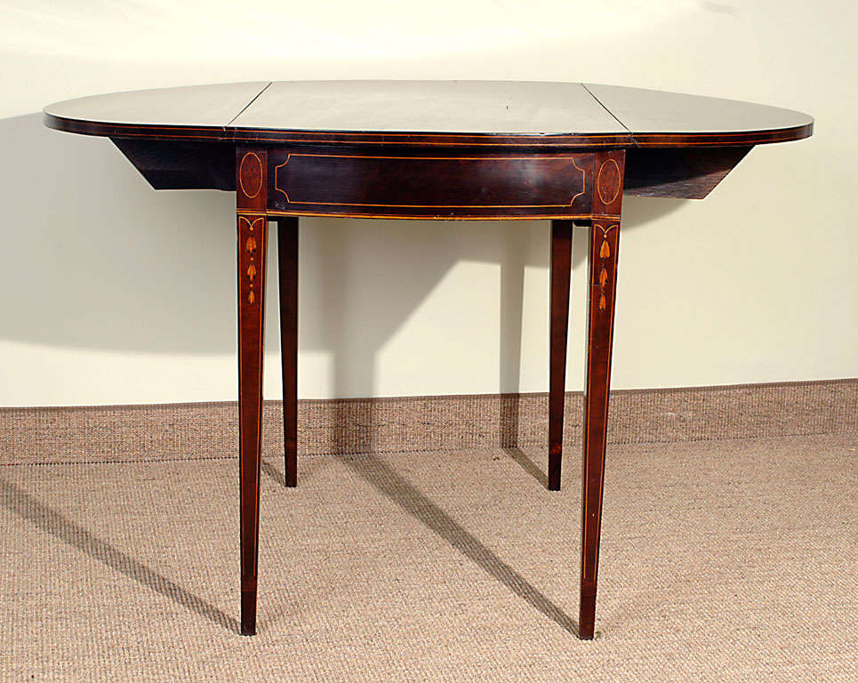 The shaped top with molded edge with D-shaped drop leaves with graduated bell flowers and string border inlay above a rectangular case with bowed ends, resting on tapering line-inlaid legs ending in cross-banded cuffs. (34.5
