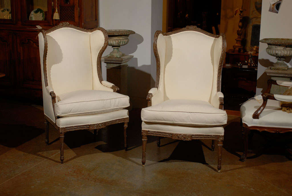 A pair of French Louis XVI style wooden wingback bergères chairs from the second half of the 19th century with new upholstery. Each of this pair of French 'bergères à oreilles' features a wing back, carved with a twisted ribbon motif on the upper