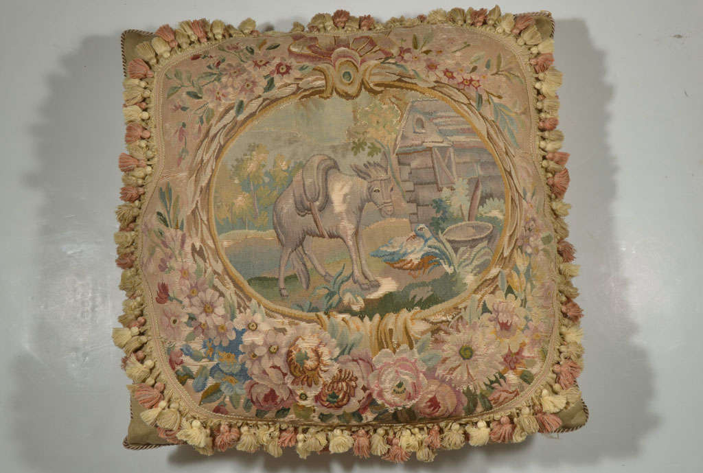 This large antique tapestry depicts a barnyard. The owners favorite pet donkey, the barn and the donkey's friend the duck are framed out in this beautiful aubusson tapestry. It is surrounded by floral bouquets. We have trimmed in in a pretty