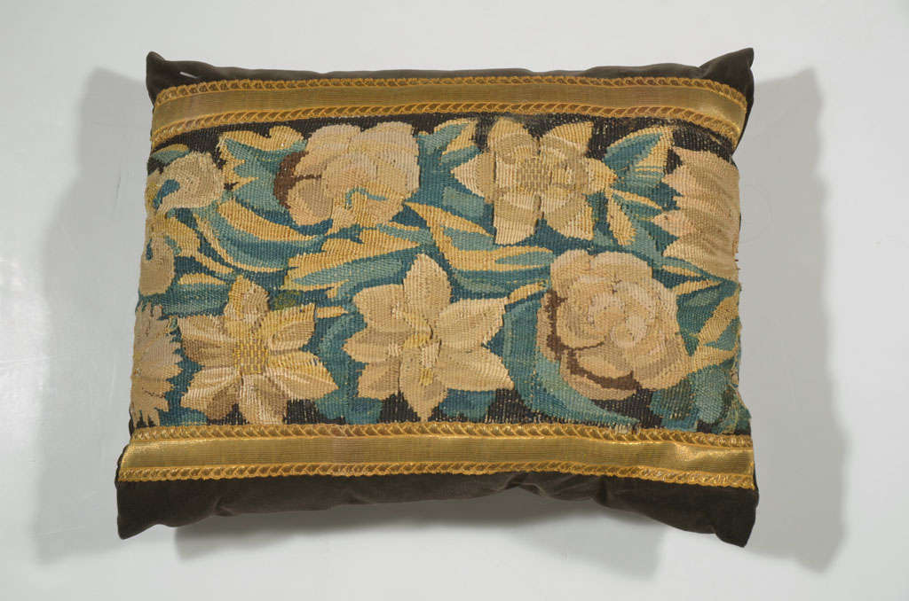 18th century antique floral tapestry fragment pillow. This pillow depicts beautiful peach, blues and greens in its floral array. It is trimmed in an antique galon ribbon and backed in a dark mushroom colored velvet.