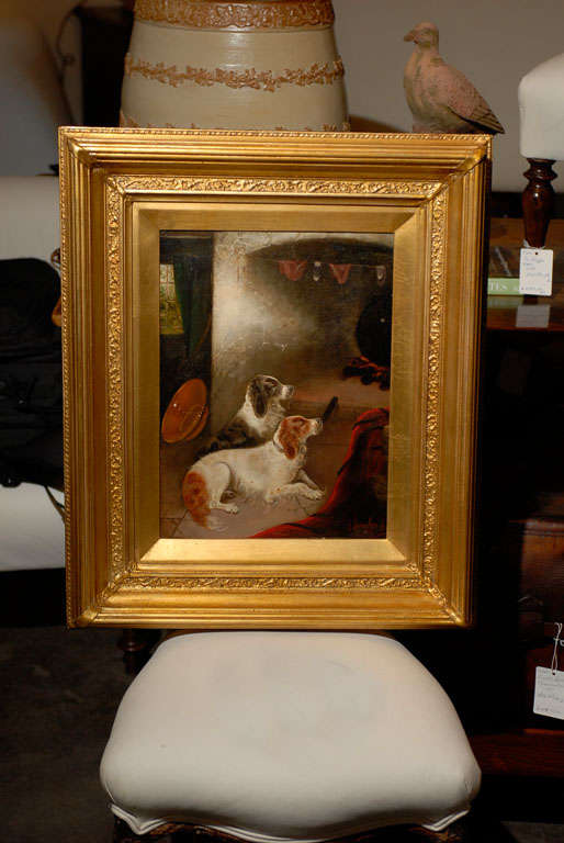 This 19th century oil painting, framed in a rectangular giltwood molded and carved frame, depicts two reclining spaniels in an interior. Resting in front of the fireplace, both dogs seem to be enjoying the warmth of the cooking pot after a tiring