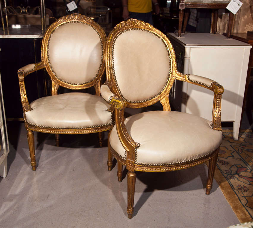 Pair of lovely French fauteuils in the taste of Louis XIV, circa 1940s, the frame beautifully gilded, oval back upholstered in beige leather, padded arm and seat, raised on fluted legs. By Maison Jansen.