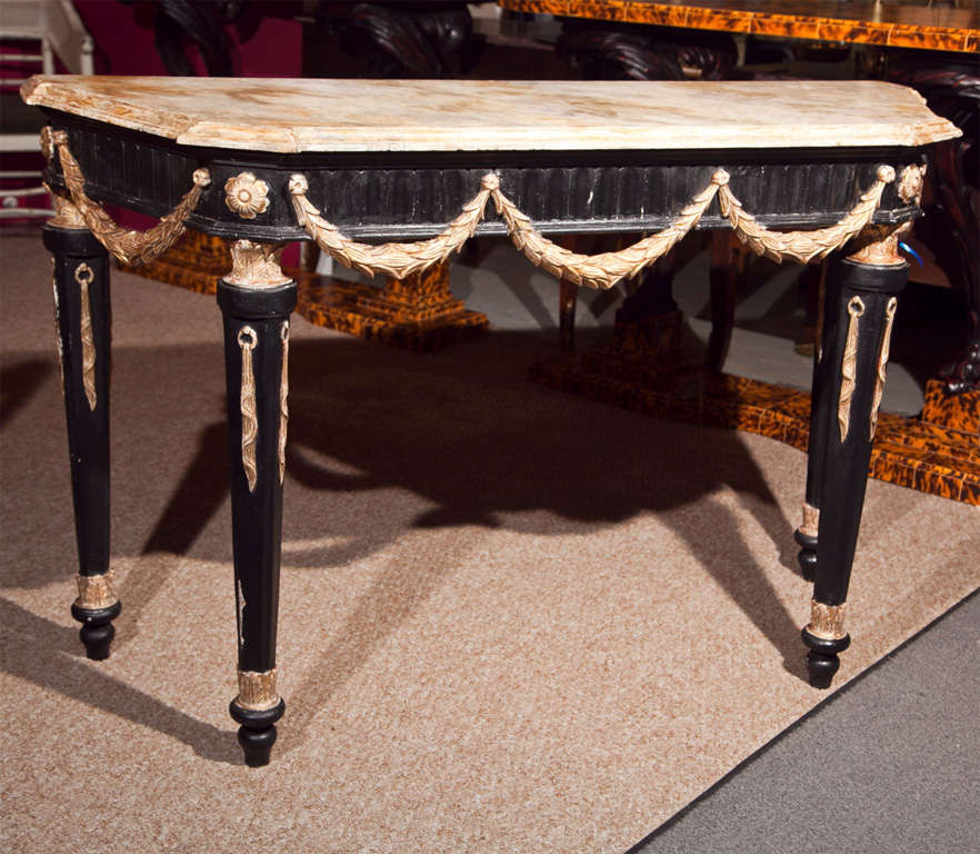 French Empire style console table, circa 1940s, painted faux marble atop an ebonized and parcel-gilt frieze decorated with wreath garland, raised on four tapering legs and toupie feet.