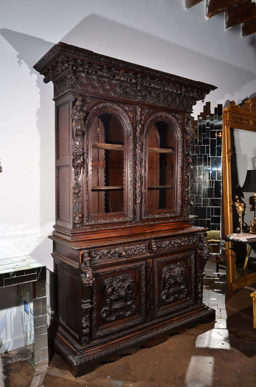 Intricately carved cupboard with various detailed references to aristocratic gluttony and plentitude. Windowed cupboard has three shelves. The entire piece is exquisitely crafted.