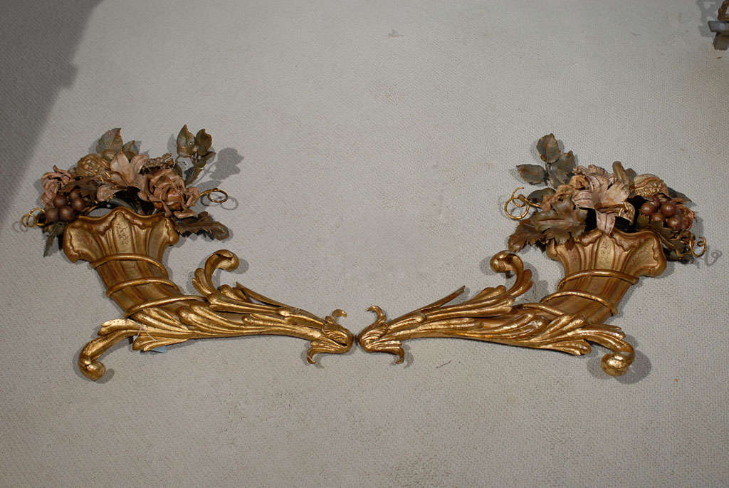 Magnificent pair of tole cornucopia wall sconces by Jansen featuring fruit and flowers spilling from a gilded iron basket. There is a light socket behind each sconce.