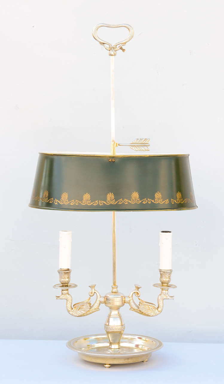 Bouillotte lamp, having an adjustable oval green tole shade with gold anthemion and scroll details, two lights, on swan arms, on round bowl base, raised on ball feet.

Stock ID: D2631