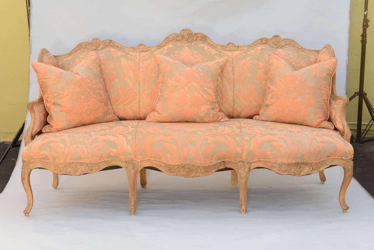 Fantastic Louis XV sofa, its original raw bleached wood frame elaborately carved on all surfaces with floral and acanthus leaf designs, upholstered in exquisite Fortuny fabric, raised on eight cabriole legs, ending in scroll toes. Accompanied by