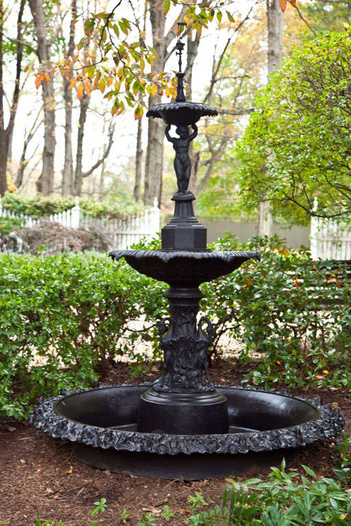A fine cast-iron two-tiered fountain, the lower baluster of egret form, the central baluster of cherub figural form, the bowls with scalloped edges, the original ground basin with foliate rim. This fountain pattern was made by a variety of American