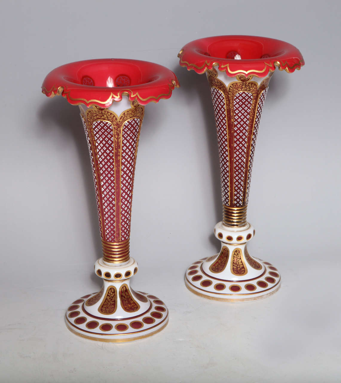 A fine pair of antique Bohemian, white over ruby red hand diamond cut, double overlay glass vases. Further beautifully decorated with 24-karat gold. Each modeled with very elaborate circular bases finely cut with cartouches, and the most beautiful