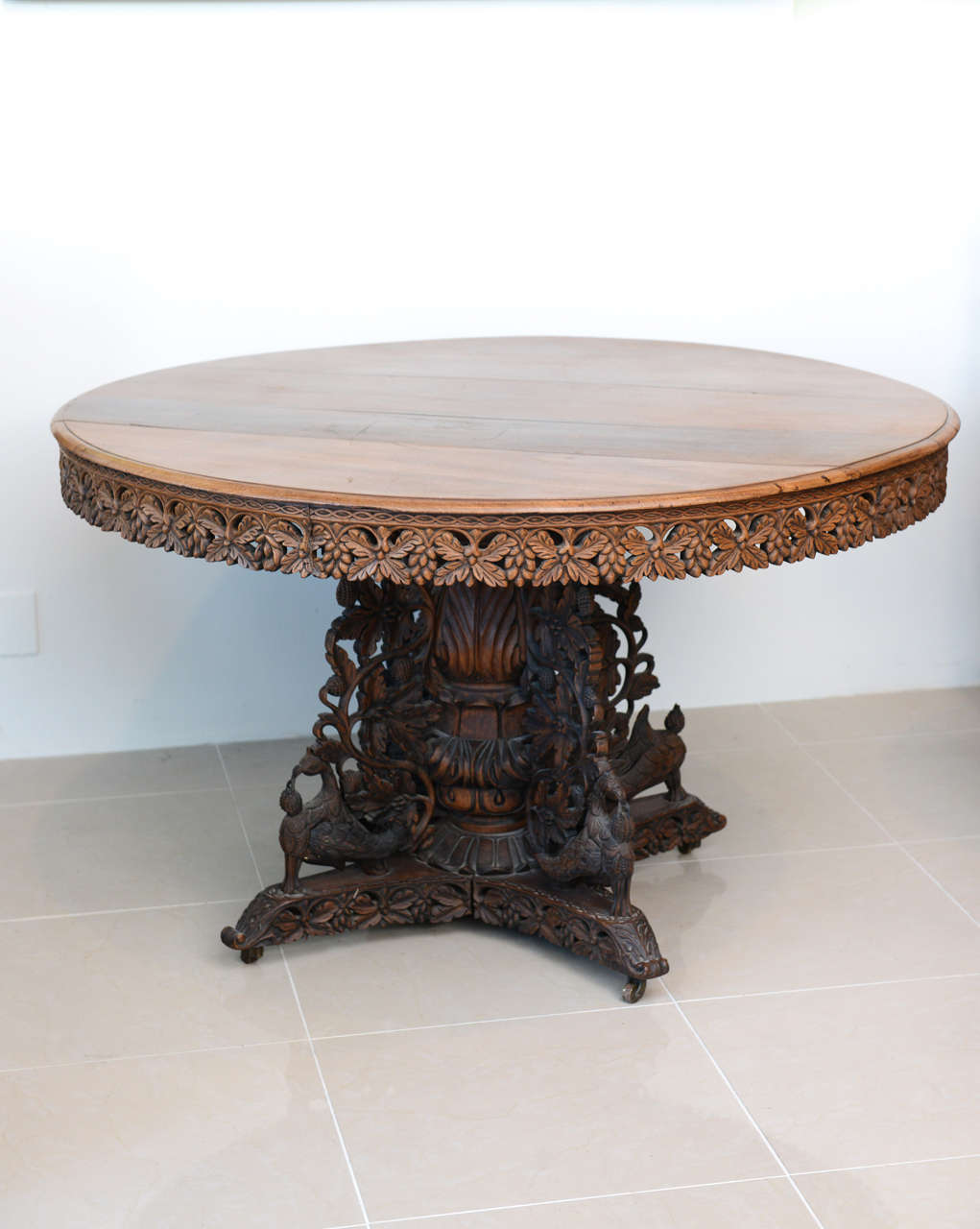The round top with a carved frieze in leaf and berry motif above an elaborately carved base with peacocks and scrolling, the top with original tilt-top hardware.