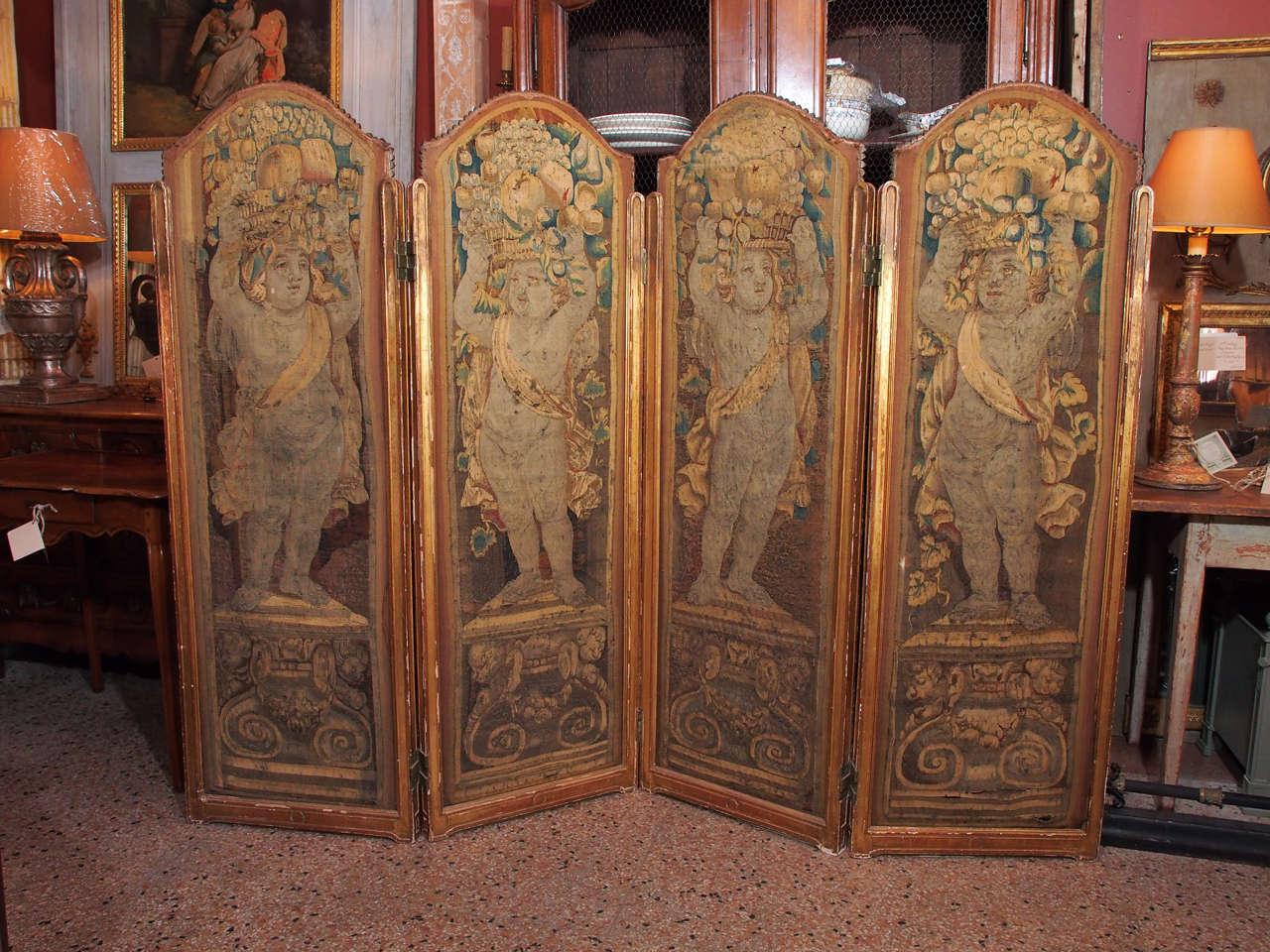 Four polychrome Aubusson wool panels. Each panel is in a giltwood frame and conical tacks holds the tapestry at the top. Each panel features a putto standing on a plinth and holding a basket of fruits on its head.