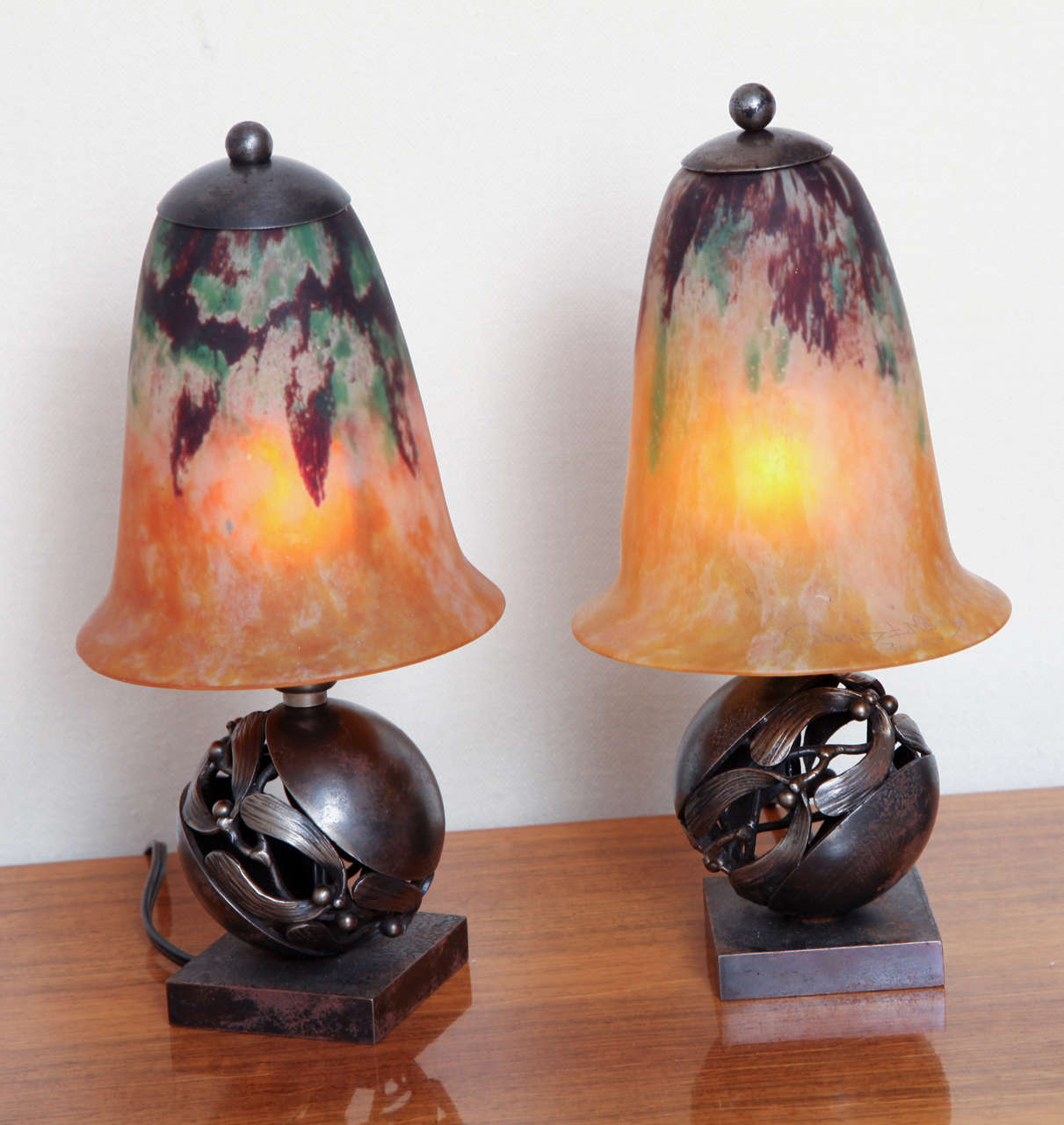 Edgar Brandt & Daum Nancy
French Art Deco pair of table lamps, with pierced spherical wrought iron bases and decorated with garland of mistletoe. Marbelized glass shades with orange and green tones, circa 1925. Similar model reproduced in: Joan