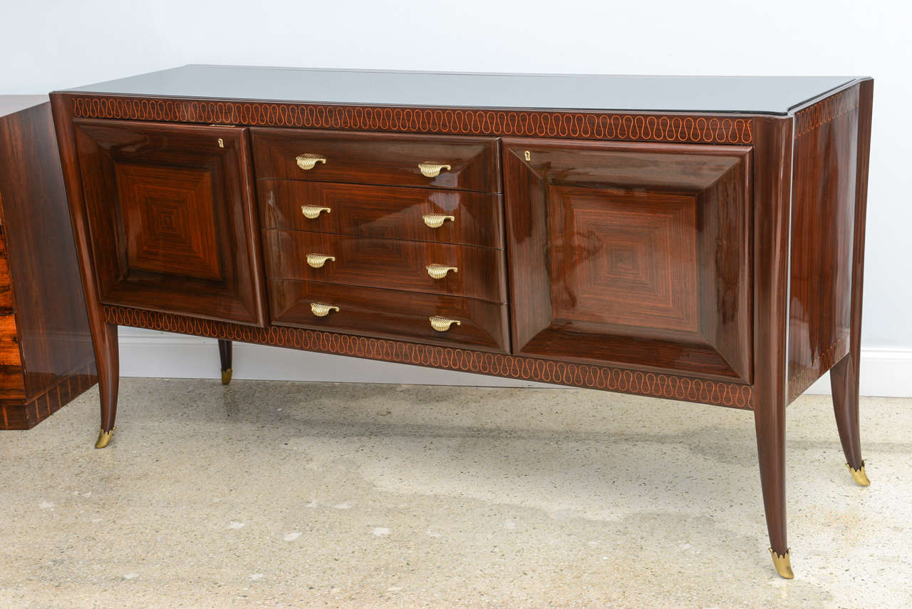 The inset black glass top with reverse decoration over a frieze with finely inlaid mixed woods over a central drawer bank and flanked by paneled doors on splayed legs with finely cast bronze sabots.