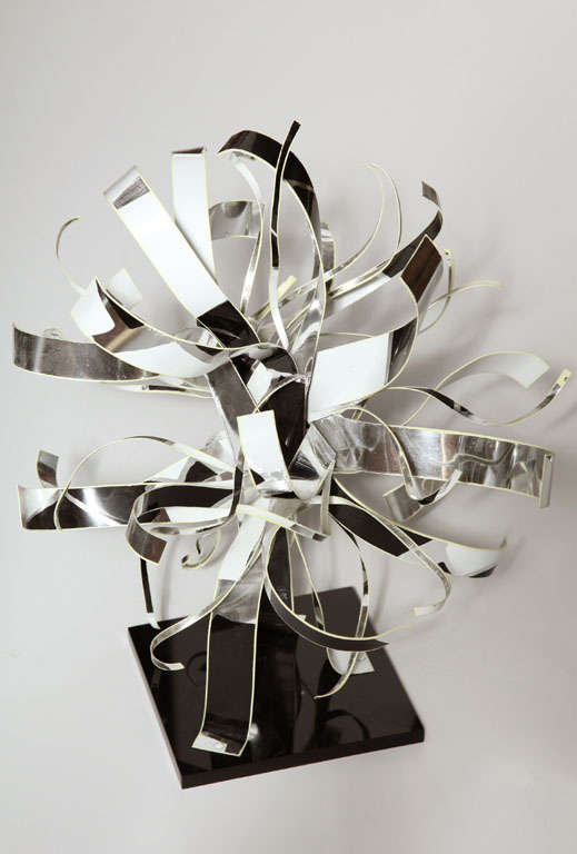 1989 Reflective Black and White Ribbon Table Top Sculpture by Dorothy Muriel Gillespie. Featuring stiff, shiny Silver bent Aluminum Ribbons with Black and White enamel on a square 6.5D Black Plexiglas base. Dimensional. Modern. Bright. Sculptural.