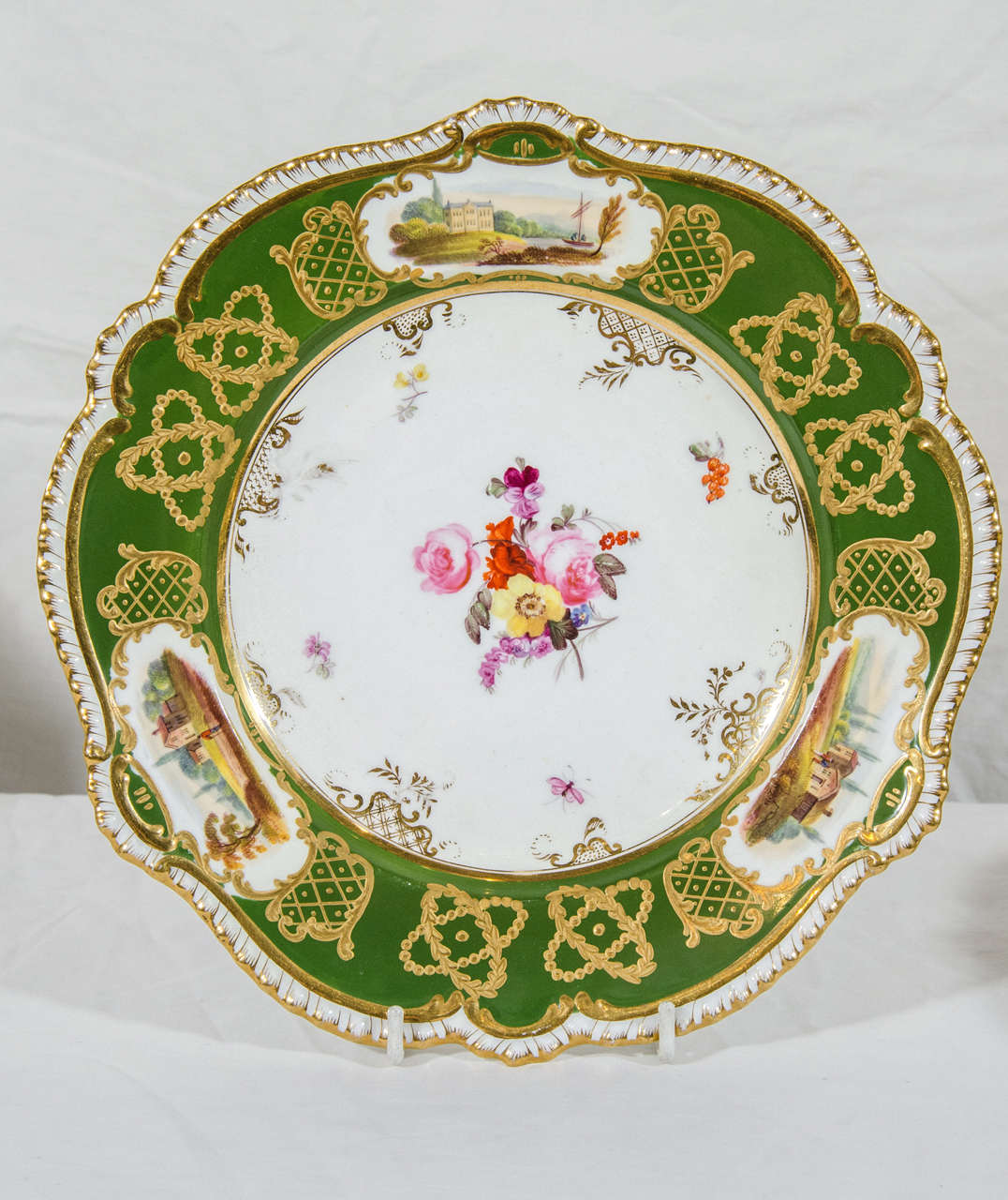 The center of each dish is hand-painted with an individual bouquet of flowers.
The wide forest green border is decorated with gilt and painted landscape scenes, all framed by a gadrooned and gilded edge.