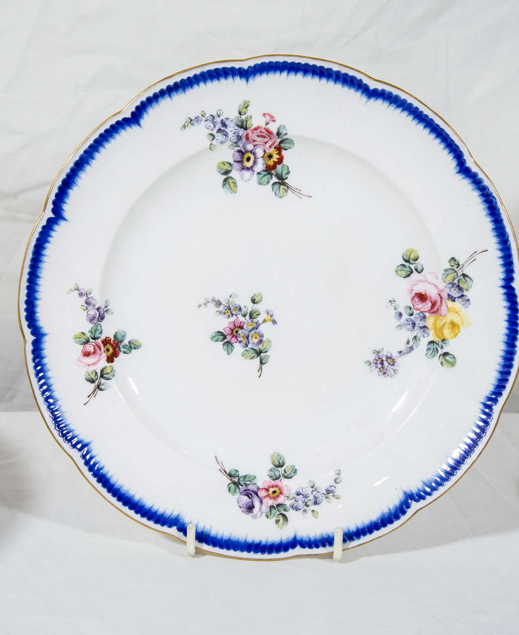 A set of a dozen 18th century exceptionally beautiful Sèvres soft-paste porcelain dinner plates decorated all-over with loose bouquets of flowers within blue enamel Feuille-de-Choux borders, and gilt-line rim on a scalloped edge. The base of each
