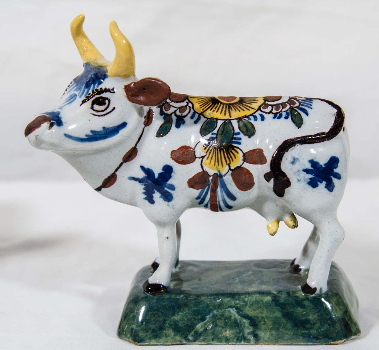 A pair of endearing 18th century Dutch Delft cows each painted with foliage, flowers, and markings in polychrome colors of yellow, iron red, and  cobalt blue. They stand foresquare on raised  green rectangular bases .