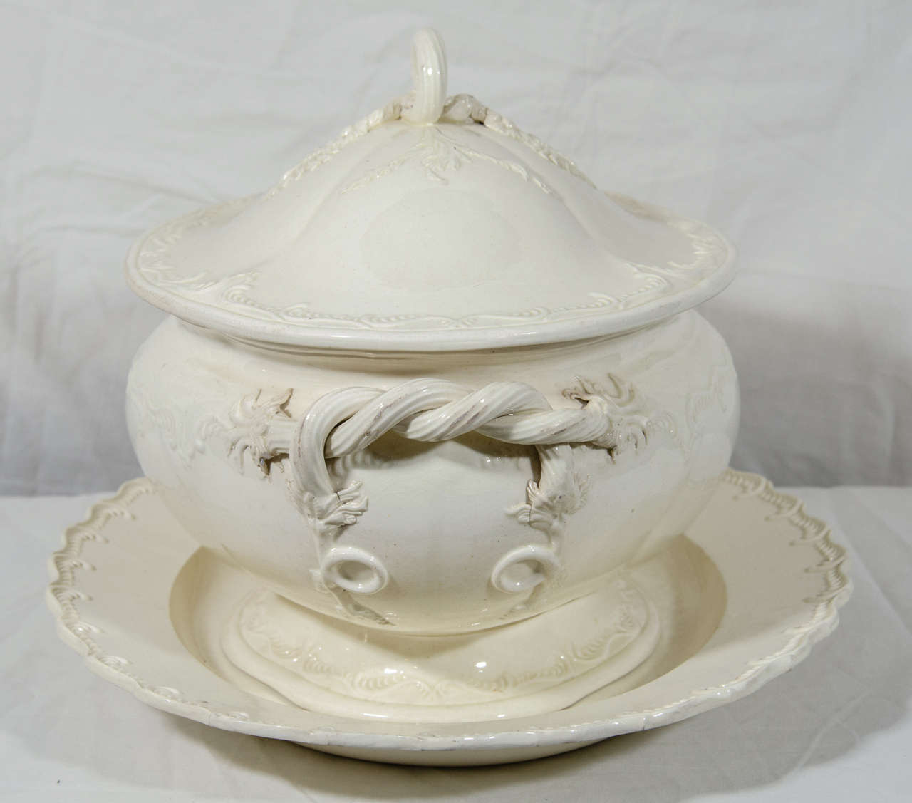 An exceptional 18th century creamware soup tureen and original stand well-proportioned and decorated with crisply molded sprigged flowers, rope handles, a looped rope finial, and feather edge borders.