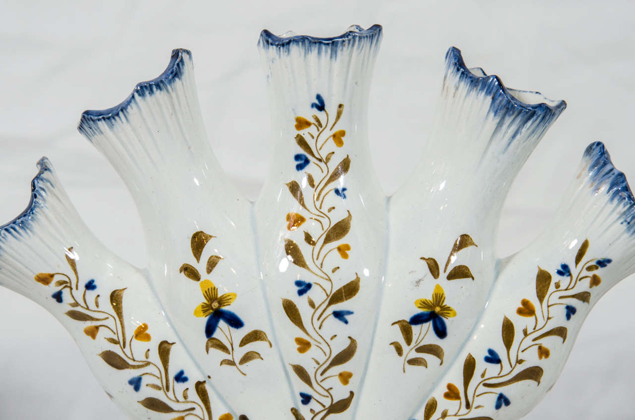 A fan-shaped pearlware tulip vase with five individual spouts for holding flowers. Decorated with leaves and flowers in prattware colors of yellow, brown and blue. The five finger vase derives its name from its similarity to a hand in the upright