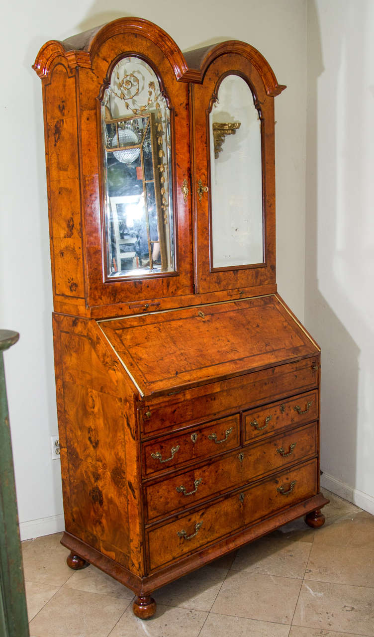 A fine and rare William and Mary burl walnut double-dome bureau bookcase with beveled mirrored doors, all-over a lower section with a fall-front revealing a fitted interior fitted with well and leather writing surface, over two short and two long