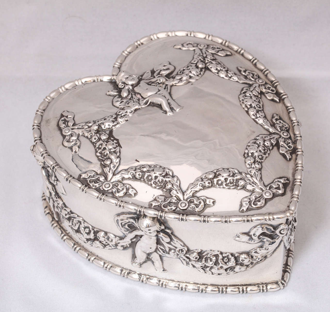 Beautiful, large, Victorian sterling silver, heart-form jewelry box (lined in burgundy velvet) with hinged lid, Howard & Co., New York, circa 1895. Decorated with cherubs, swags, ribbons and bows. No monogram. Measures: 4 1/4