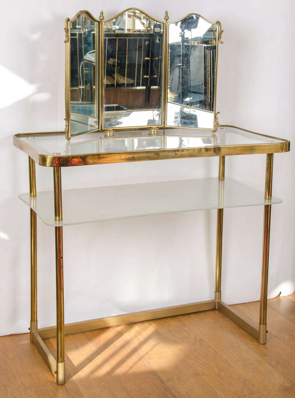 Two-tiered 1950s dressing table in brass with integral triptych mirror, the lower shelf in etched glass with a polka dot design having a switch operating a fitted light, all on a rectangular base.